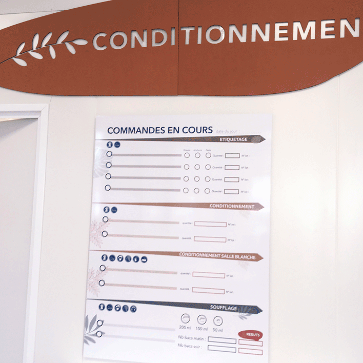 EMERAUDE ID signalétique conditionnement réalisé sur bois en creux. Le mot Conditionnement est associé à une couleur et le dessin d'un végétal lui aussi découpé en creux dans la plaque de bois. On voit également un panneau Commande en cours. Il permet aux travailleurs de savoir tout ce qu'il y a à faire et ainsi d'être plus autonome. Mot clé : design-inclusif signalétique-accessible design-d'espace